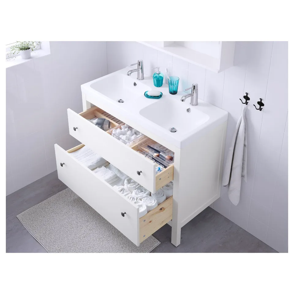 Modern bathroom sink with organised toiletries and folded towels. White cabinet, chrome tap, and blue containers.
