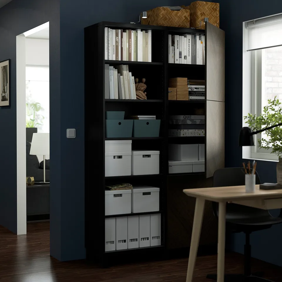 Dark wooden storage unit with multiple shelves, storing various books and containers, next to a wooden table with a chair.