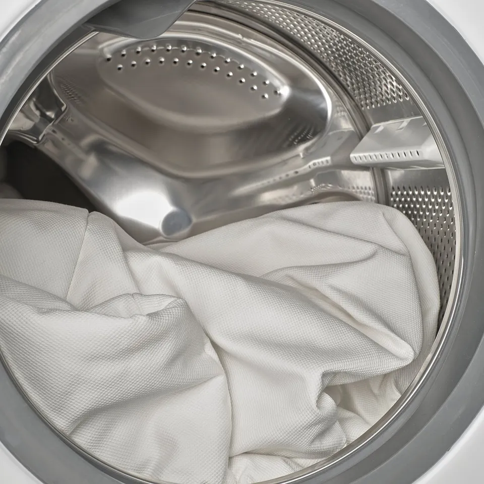 Stainless steel washing machine drum with white clothes, illustrating machine-washable feature.