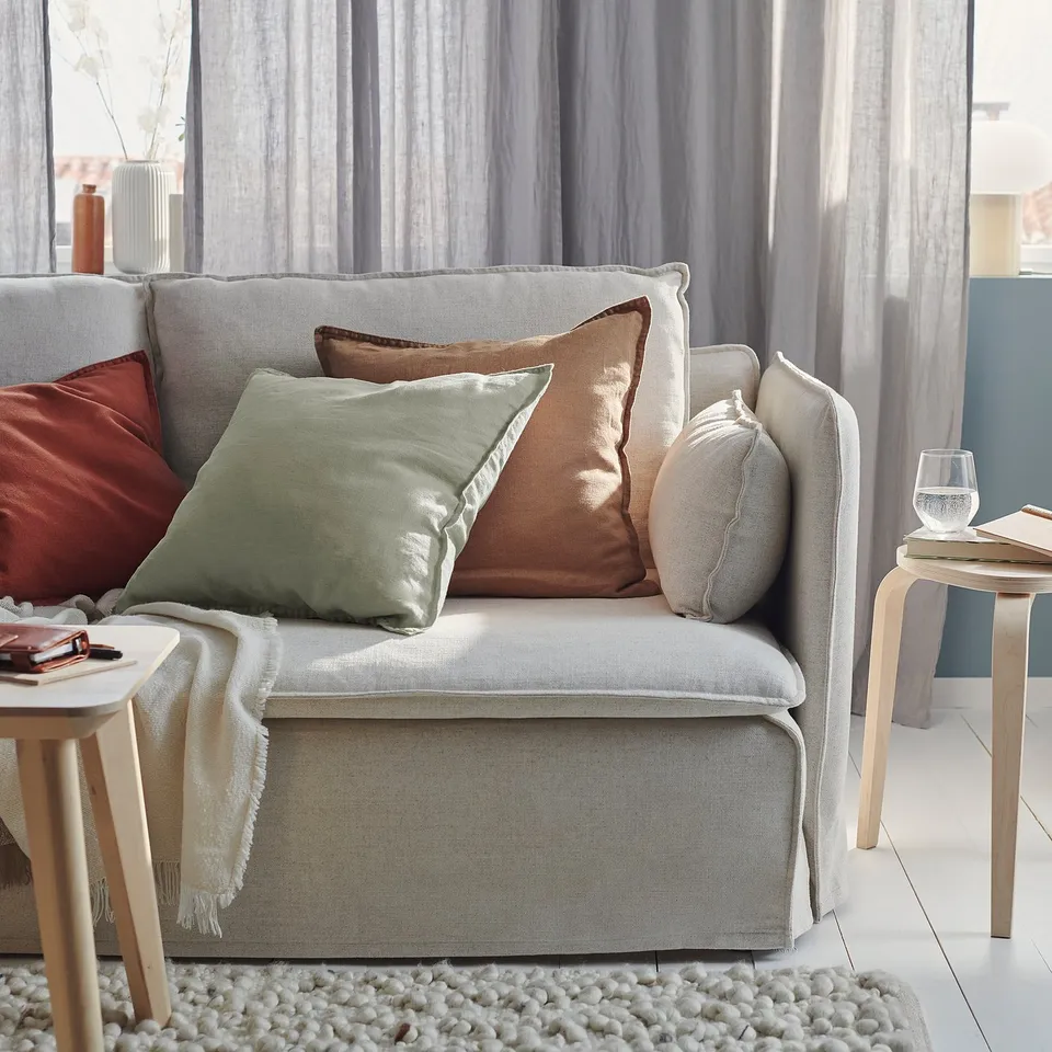 Cosy living room with grey-green linen cushions on a light-colored sofa, complemented by wooden side tables and a textured rug.