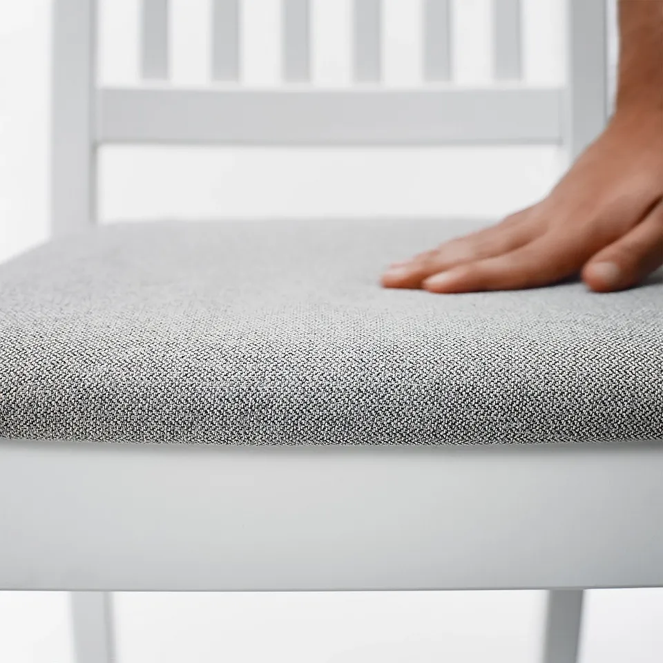 A persons hand presses a soft, fabric-covered seat cushion on a white chair.