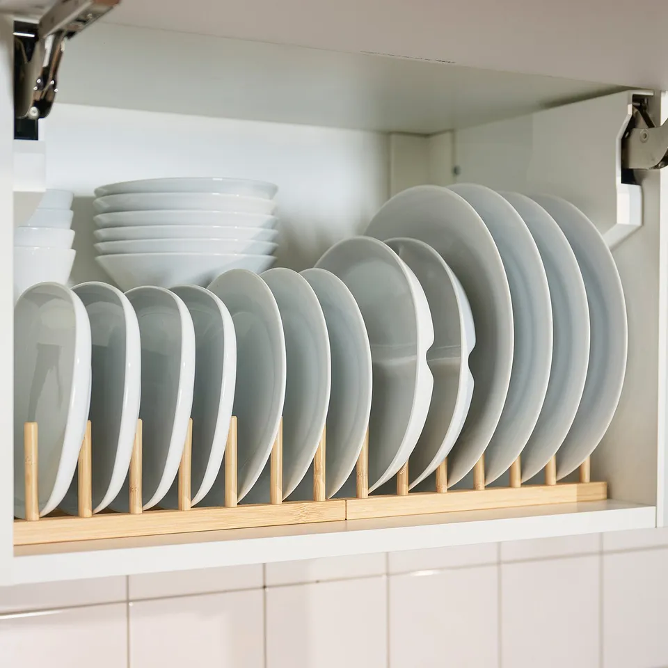 A bamboo plate rack holding multiple white plates in a kitchen cabinet, showcasing its drying and organising capabilities.