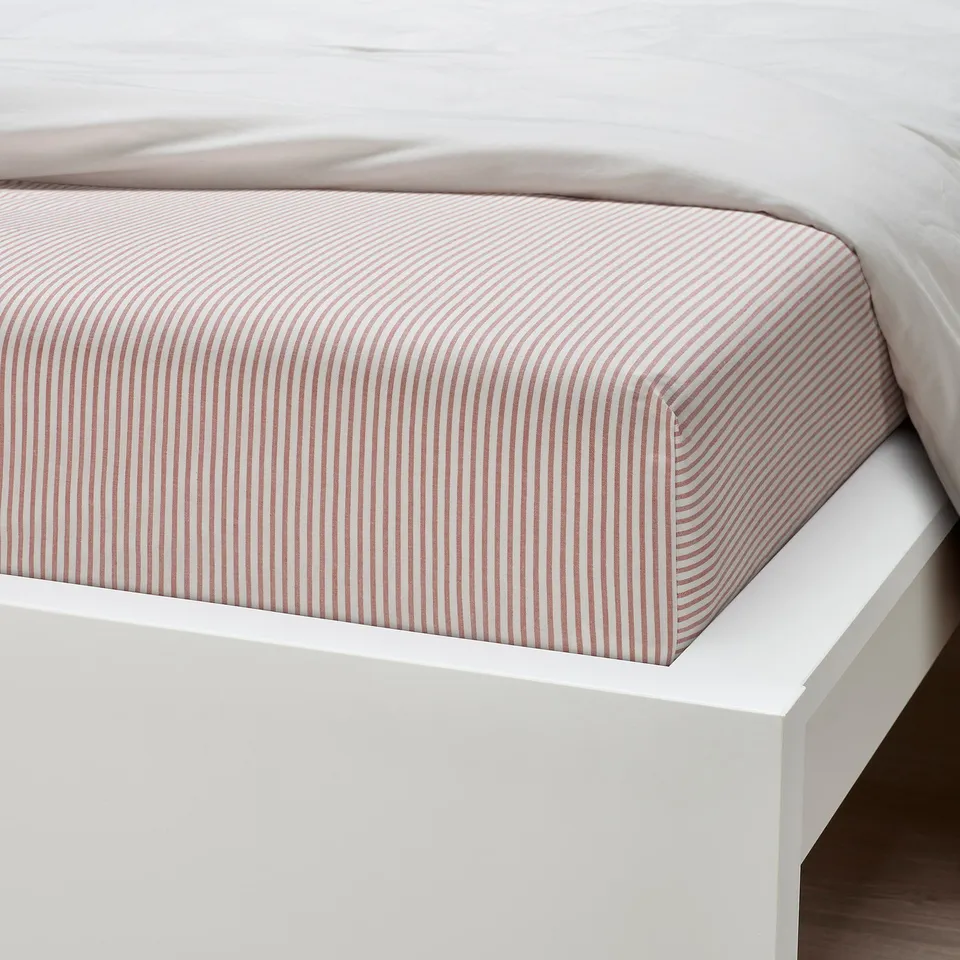 Bed with striped fitted sheet on white frame. Sheet is neatly tucked, showing quality and fit.