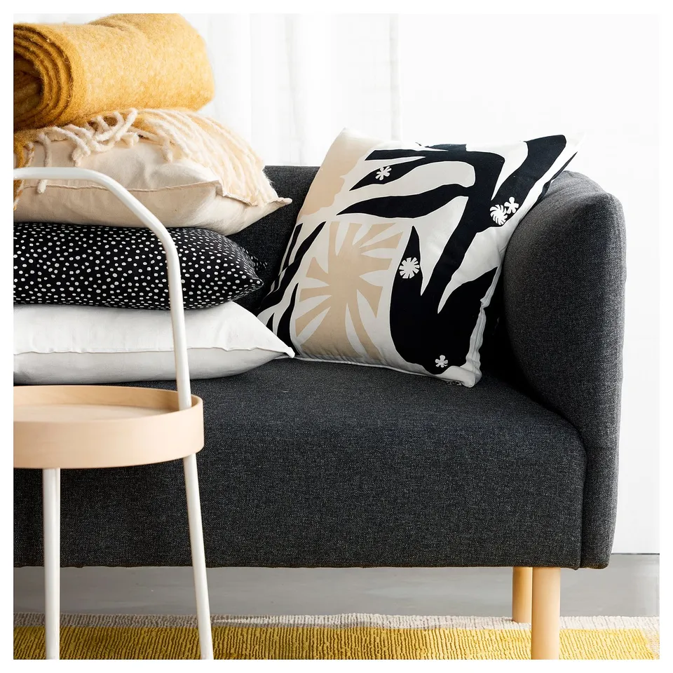 Modern living room with a dark grey sofa, colourful pillows, and a yellow rug. The central pillow on the sofa has a black and white floral design.