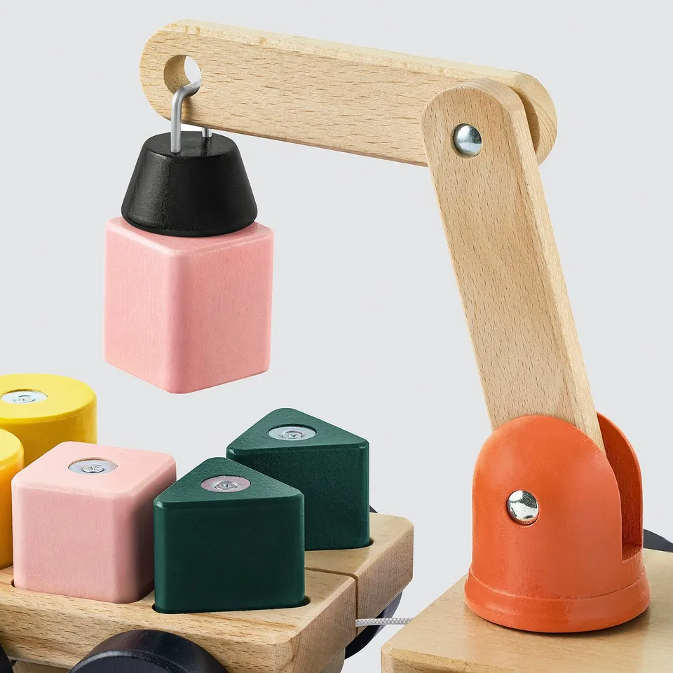Wooden toy crane lifting pink block, with other colourful blocks nearby.