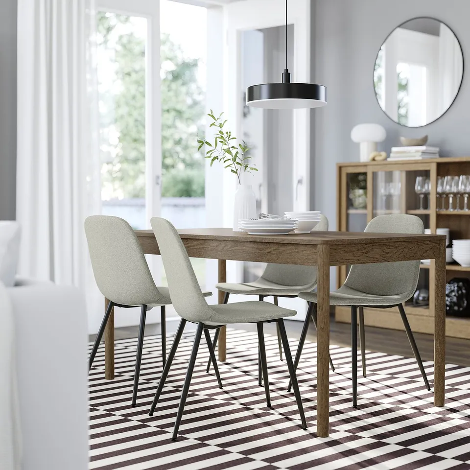Minimalist dining room with grey NORDMANSSKÄR chair, wooden table, and greenery. Bright, cosy decor with grey walls and striped flooring.