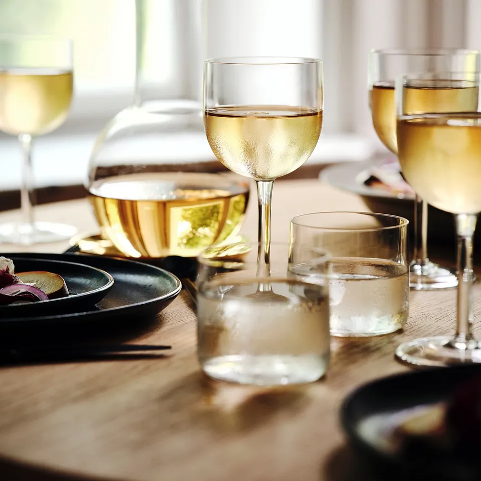 Four elegant, mouth-blown wine glasses on a wooden table, showcasing sleek design and stability, part of the STOCKHOLM 2025 collection.