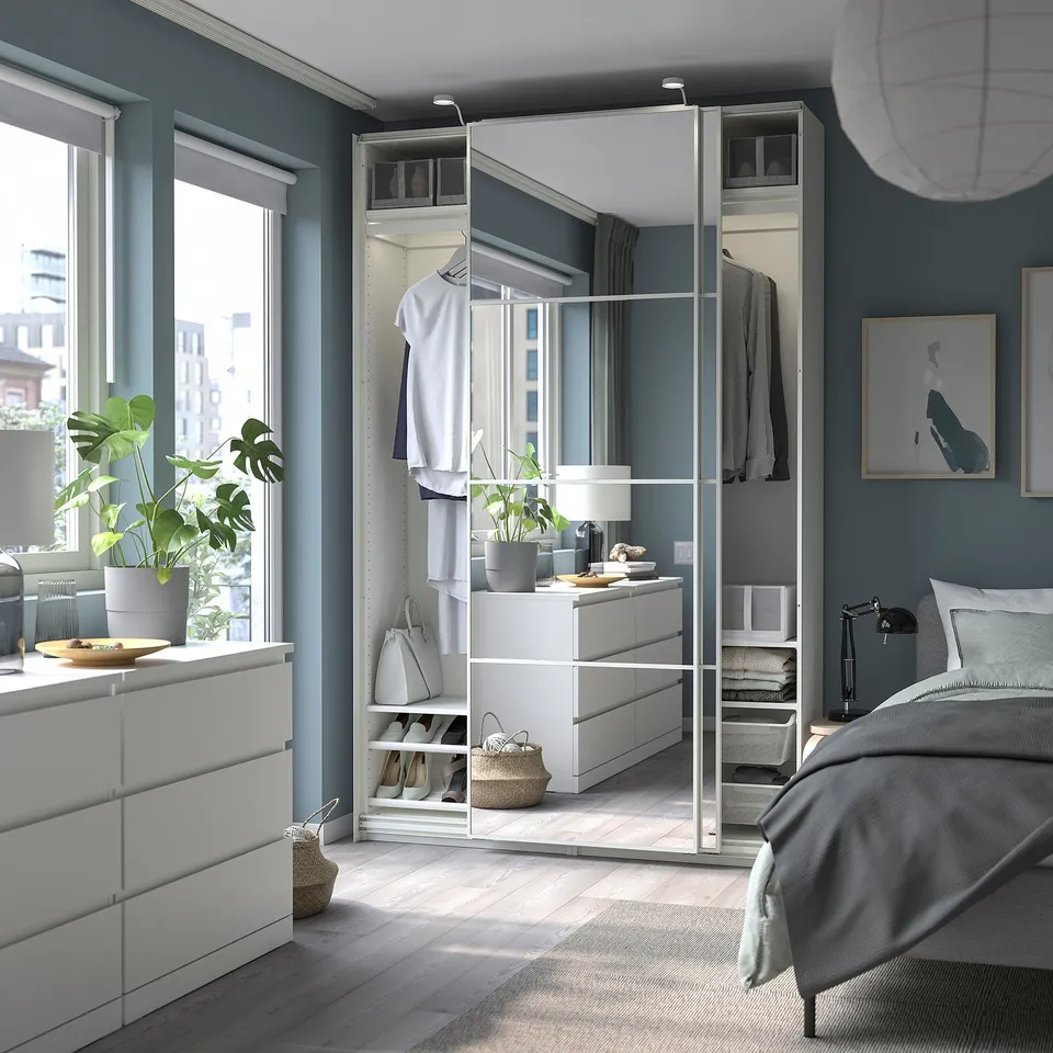 Modern bedroom with a white PAX wardrobe, large mirror, grey walls, wooden floor, bed, and plants.