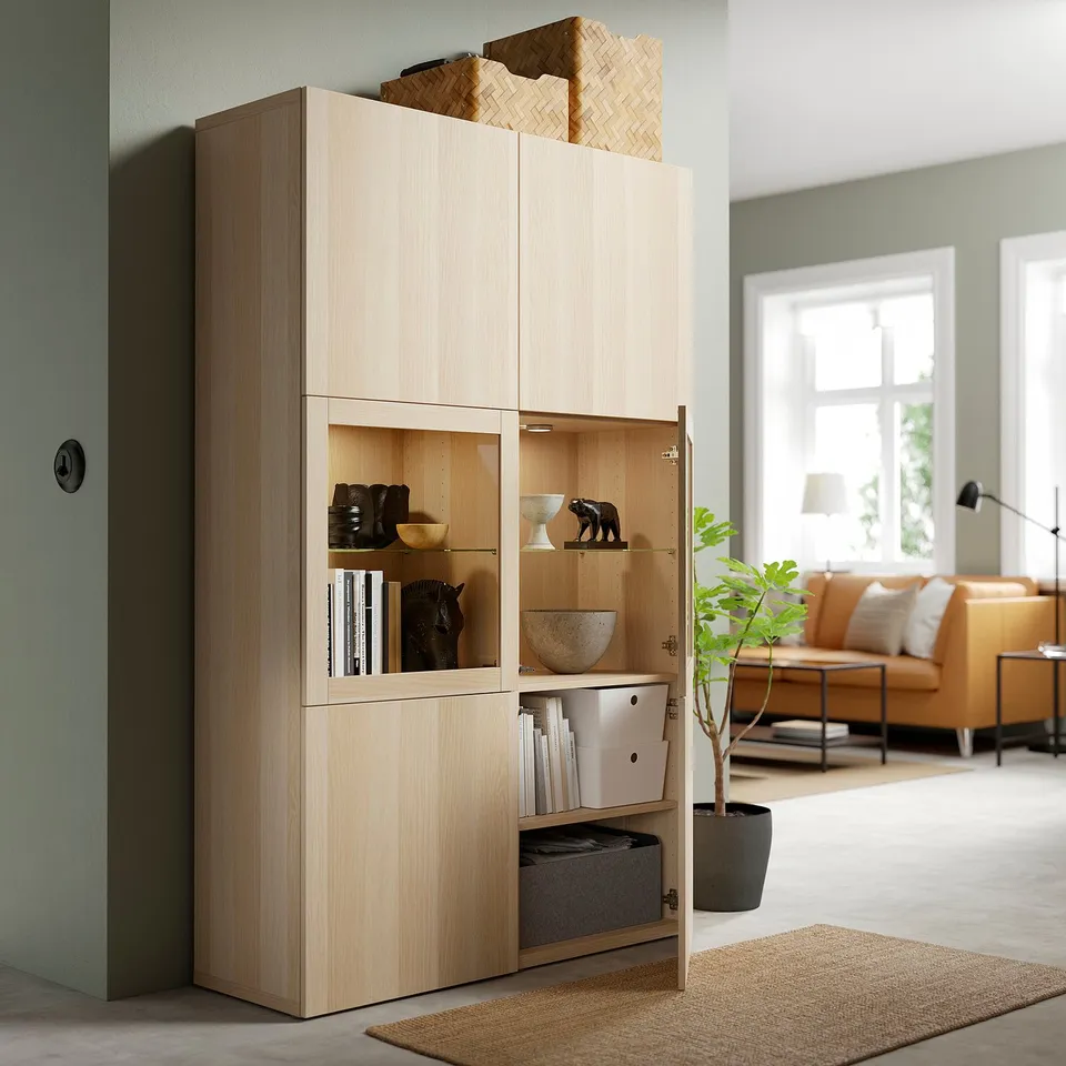 Light wood cabinet displays items behind glass doors, with open shelves showing storage boxes, situated in a living room.