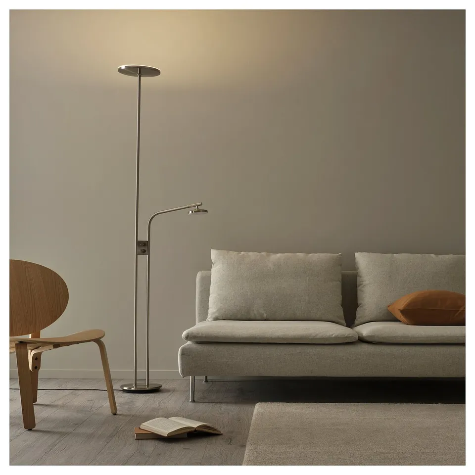 Modern living room with light grey sofa, wooden chair, and silver floor lamp with adjustable reading light. Open book on the floor.