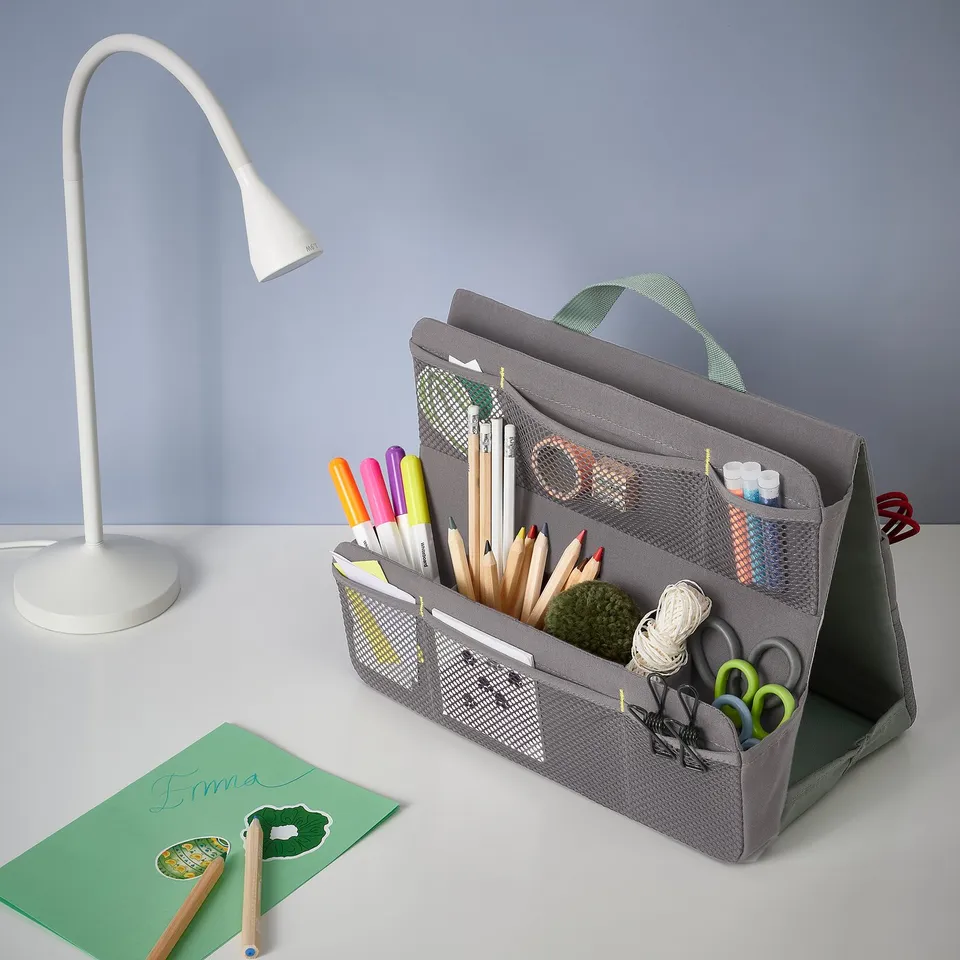 Grey fabric organiser on a desk holding coloured pens, pencils, scissors, and other school supplies.