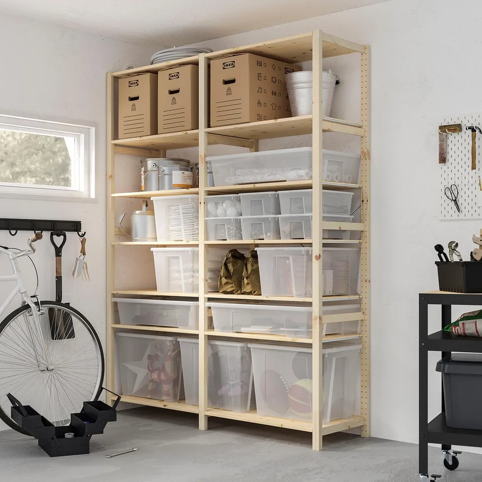 Organised garage with light wooden shelves holding clear plastic SAMLA boxes for storage. A bicycle is leaning nearby.