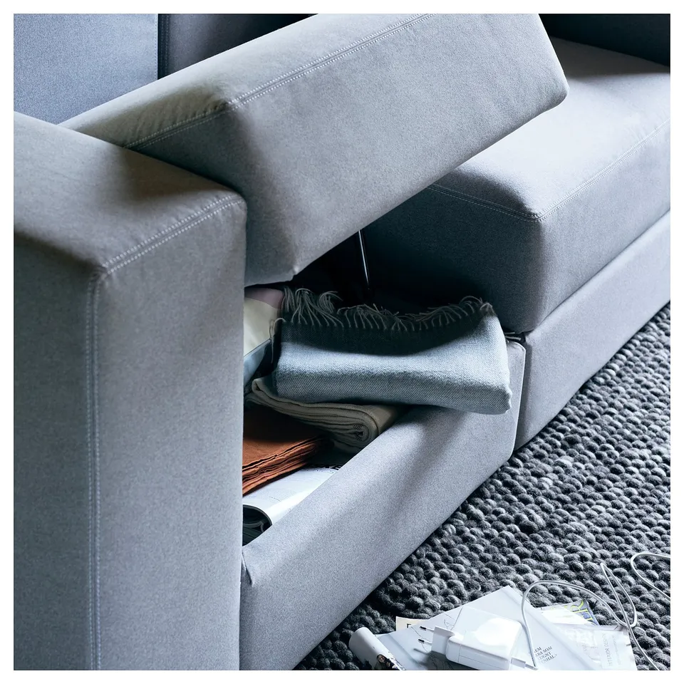 Modern grey modular sofa with folded blankets and charging station on knitted rug.