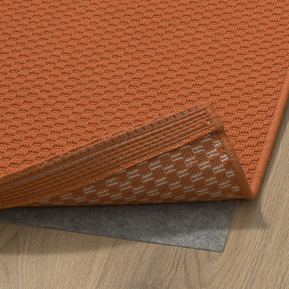 Aneurysms orange woven rug, folded, with backing, on wooden floor.