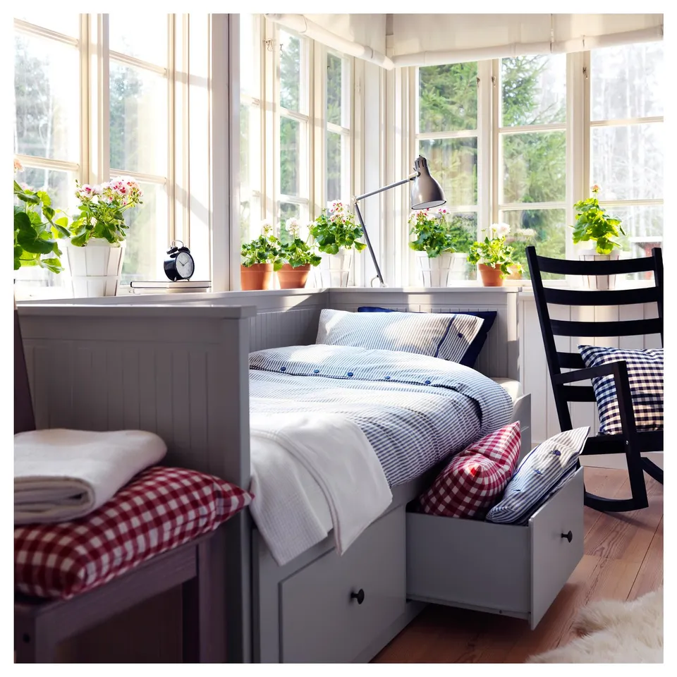 Bright, cosy bedroom with large windows; white daybed, red-and-white chequered cushions, and potted plants.