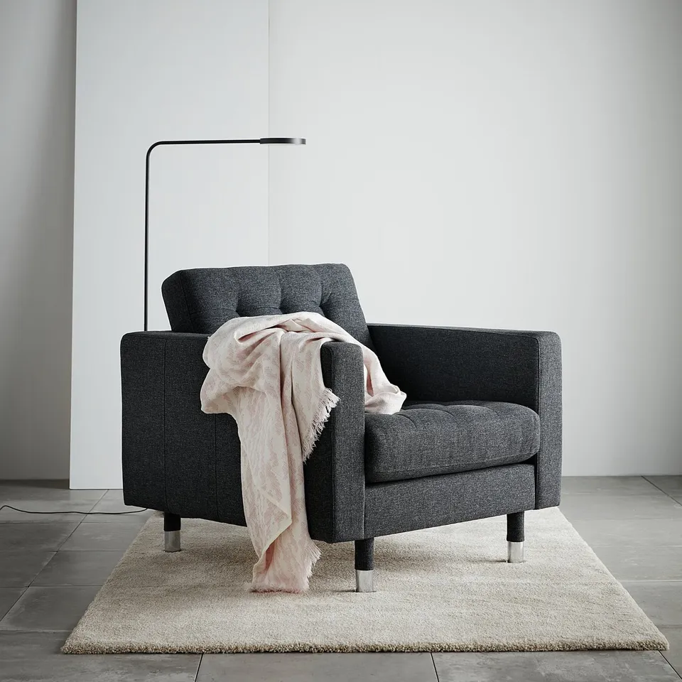 Modern dark grey armchair with light pink throw blanket and floor lamp.