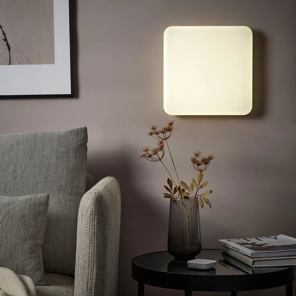 JETSTRÖM smart light panel glows softly above table with green vase and books, enhancing minimalist decor.