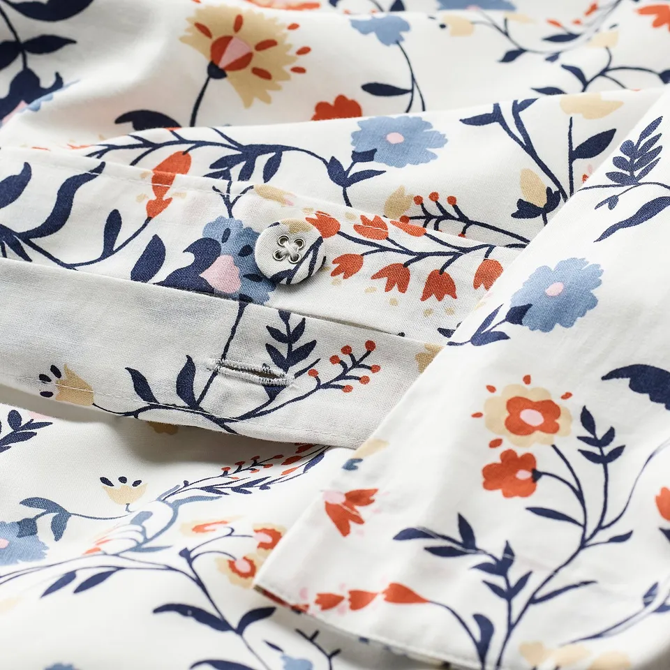 Floral duvet set with button closure, made of organic cotton, white background with multicoloured flowers, folded neatly.