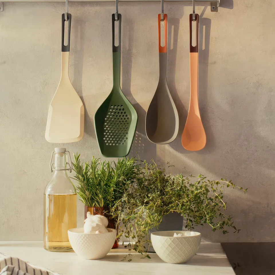 Five colourful spatulas hang neatly, ideal for flipping food with a wide, square blade. A bottle and bowls of herbs add kitchen charm.