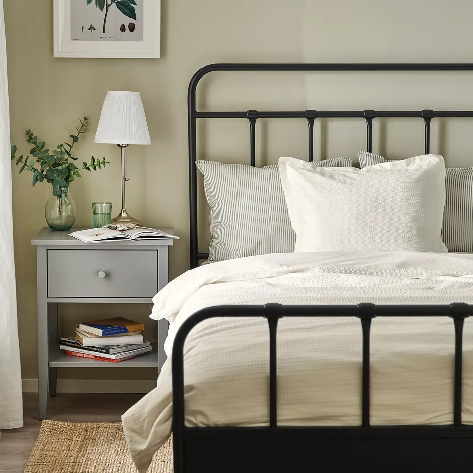 White duvet on black bed, grey bedside with books and lamp.