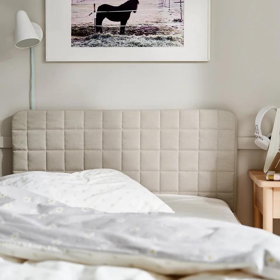 Bedroom with beige SLÄKT headboard, white bedding, framed horse photo, and wall lamp.
