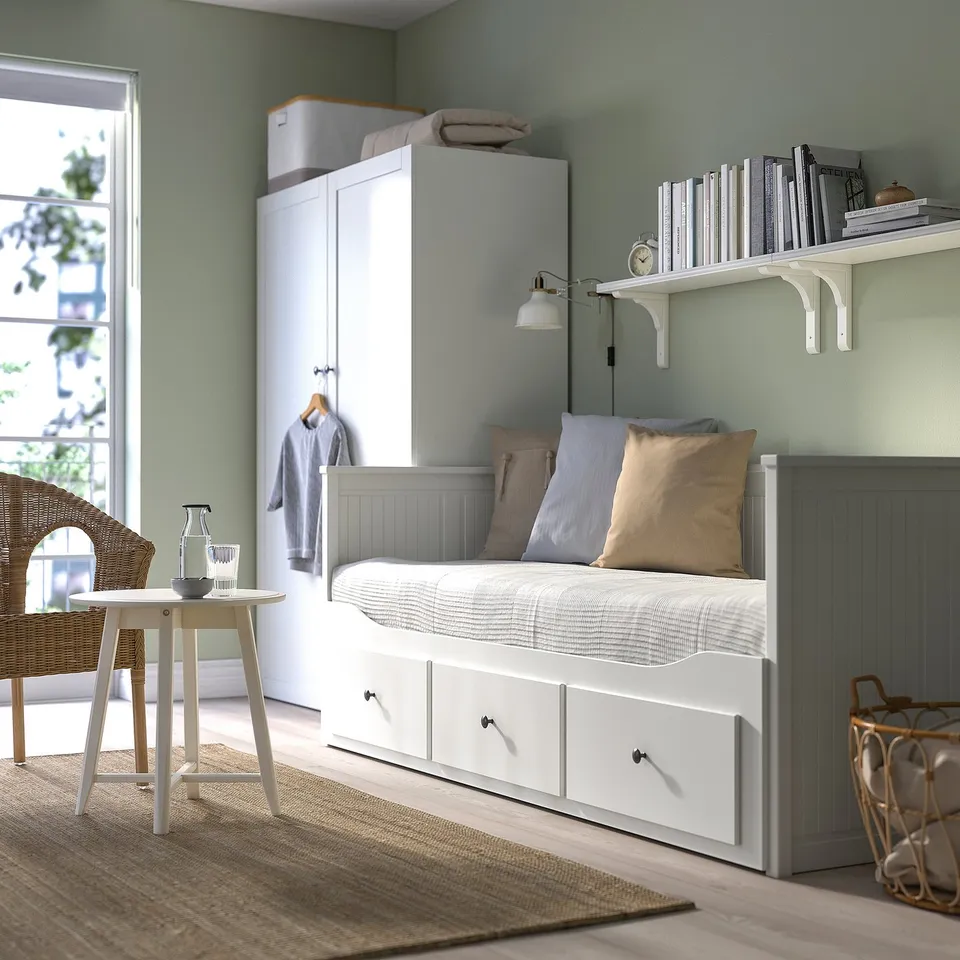 Small cosy room with white HEMNES day-bed, grey closet, and wicker chair by window.
