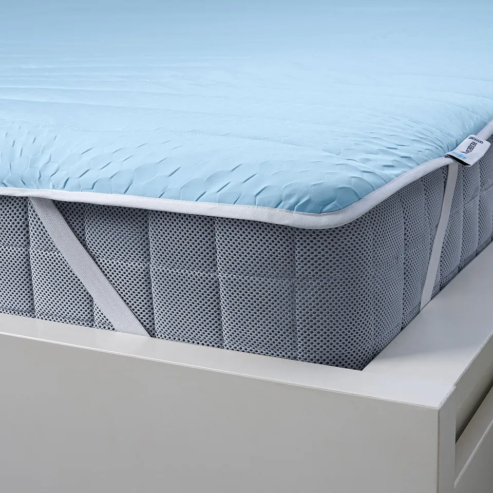 Blue mattress protector with cool-to-touch surface displayed on bed, showcasing elastic corners for secure fit