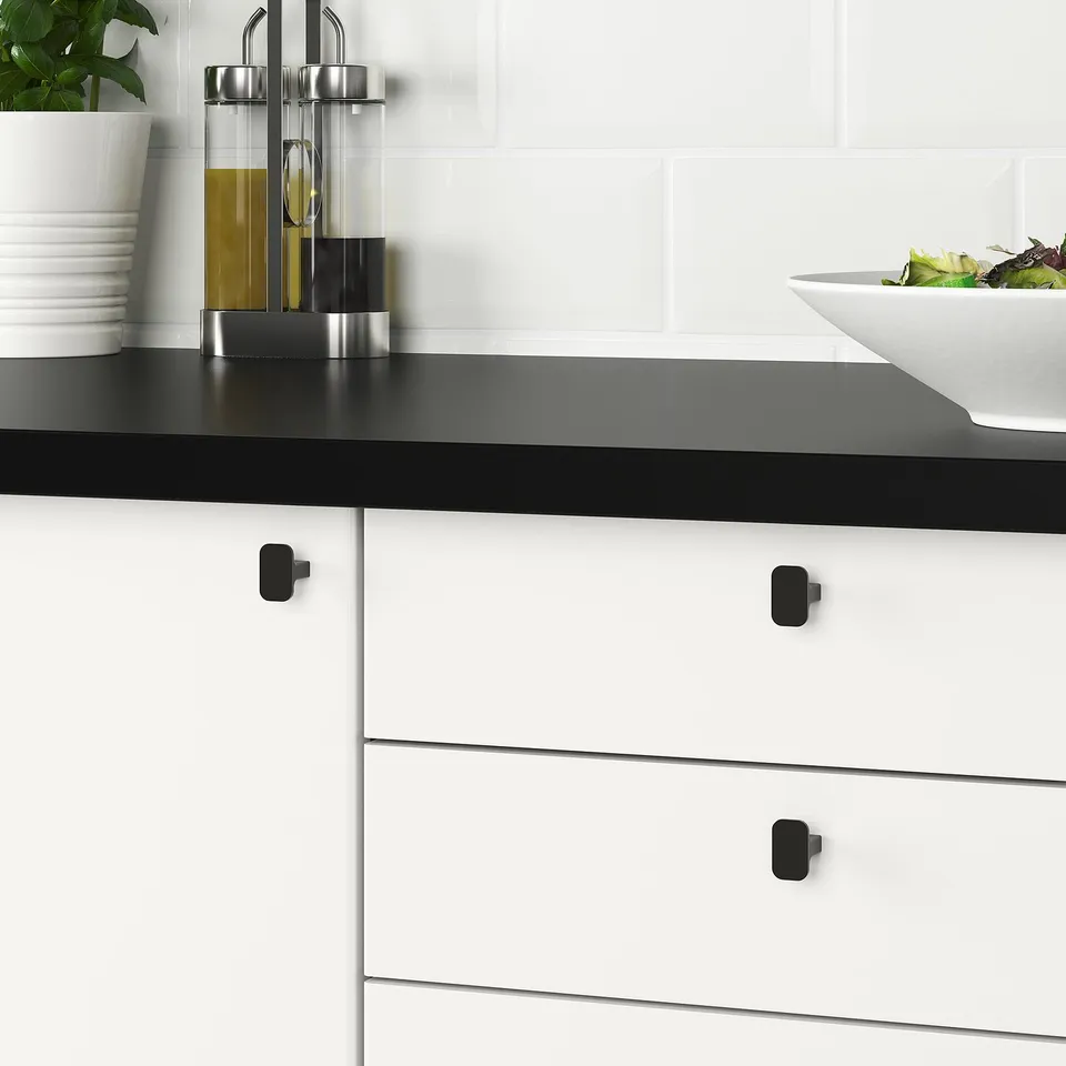 Modern kitchen with black countertop and white cabinets featuring sleek, easy-to-grip HACKÅS knobs.