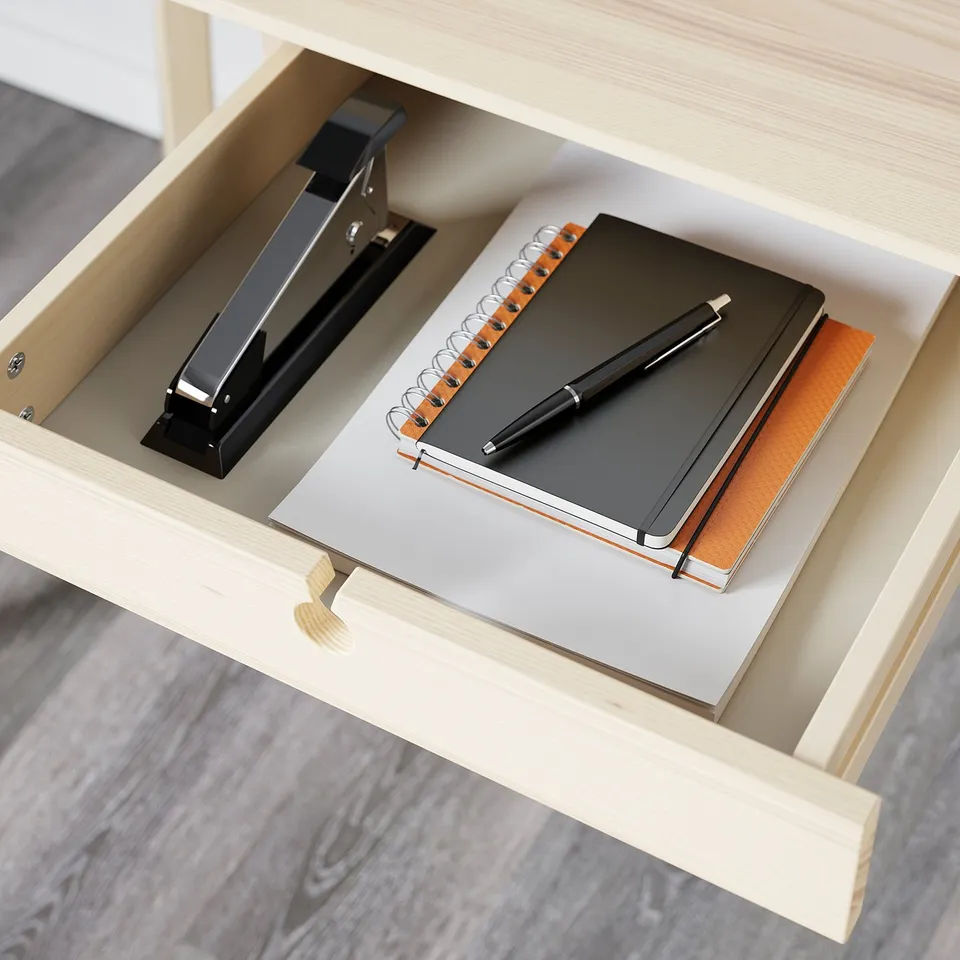 Open desk drawer with notebook, pen, and stapler, neatly organised.