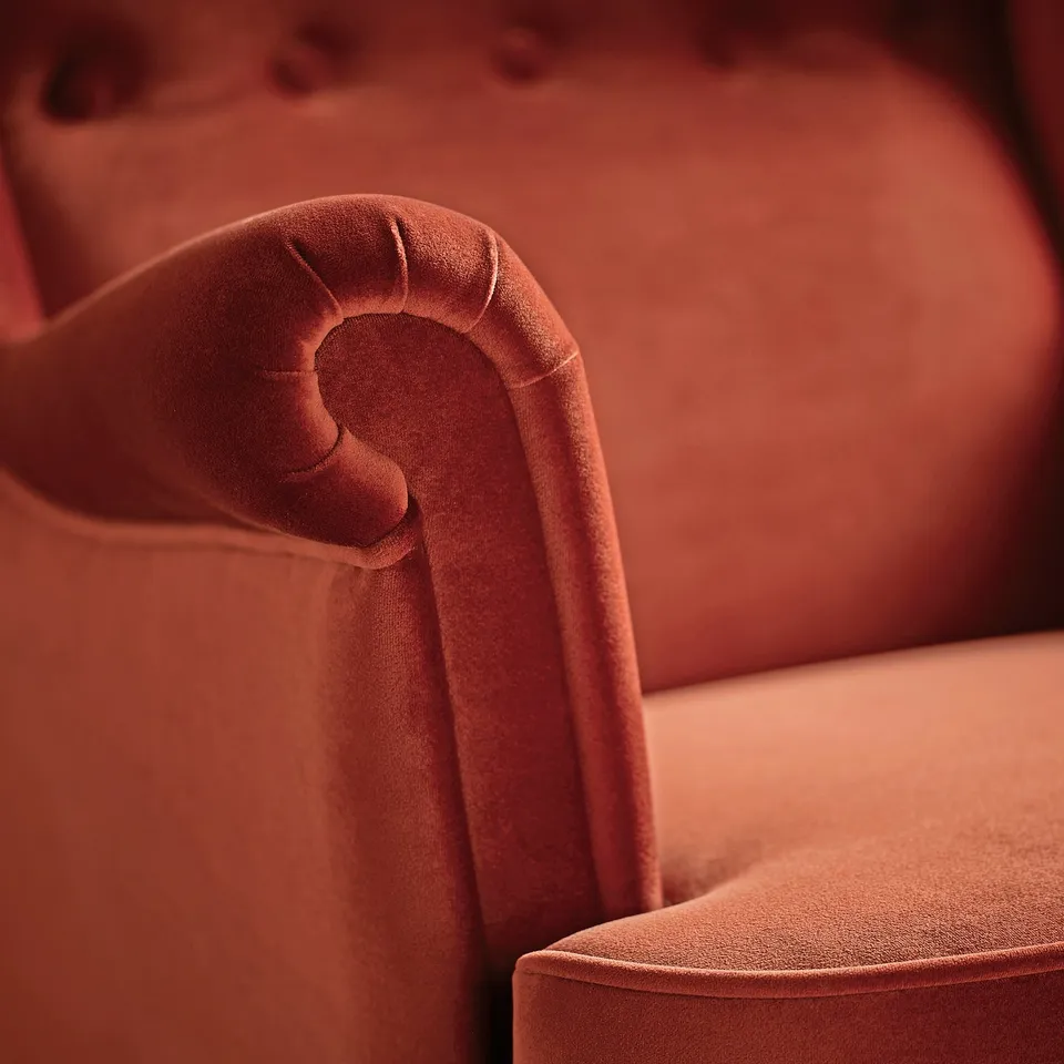 Luxurious, burnt orange velvet chair with curved back, offering soft, embracing comfort.