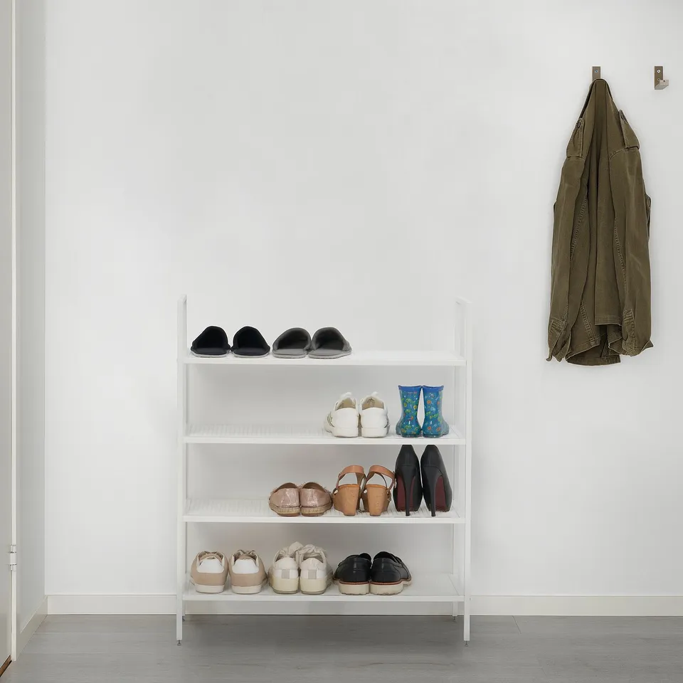 White, 3-tiered BOJTEN shoe rack, holding 16 pairs, against a wall with a hanging jacket.