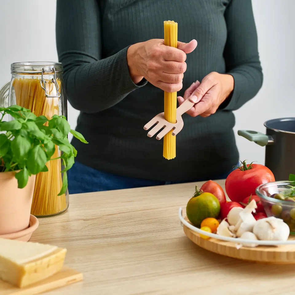 Person holding spaghetti server in kitchen with ingredients.