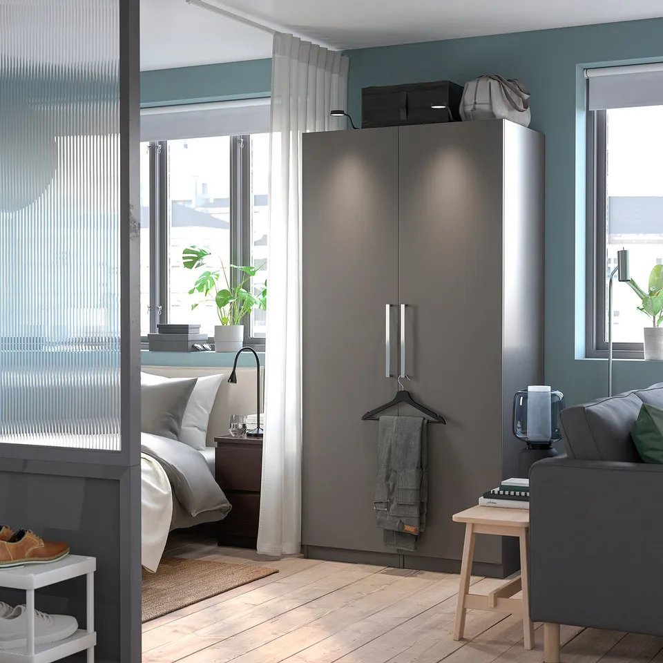 Modern bedroom with tall grey PAX wardrobe, sofa, hanging clothes, shelves, and bed.