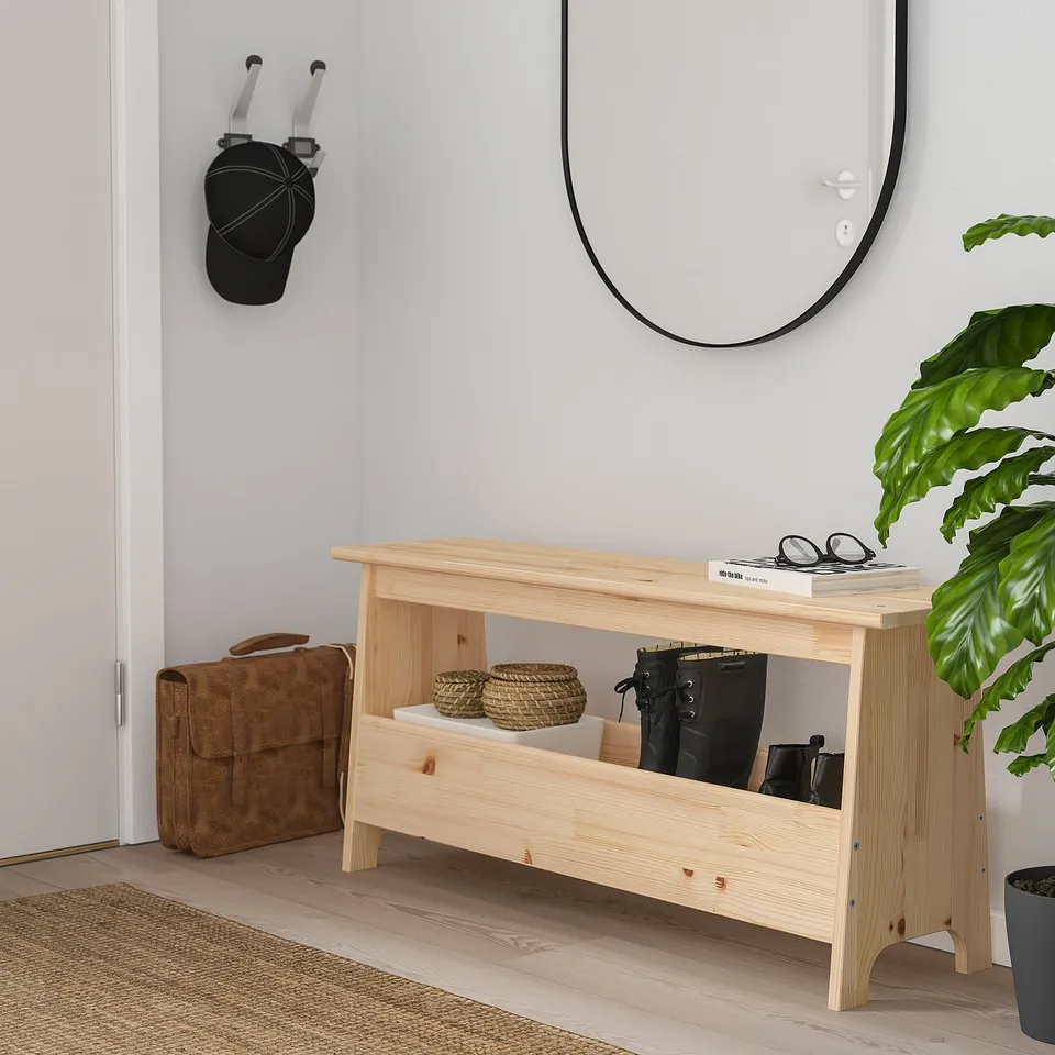 Modern, light wood PERJOHAN bench with storage fits neatly under wall mirror, beside a brown bag and large green plant.