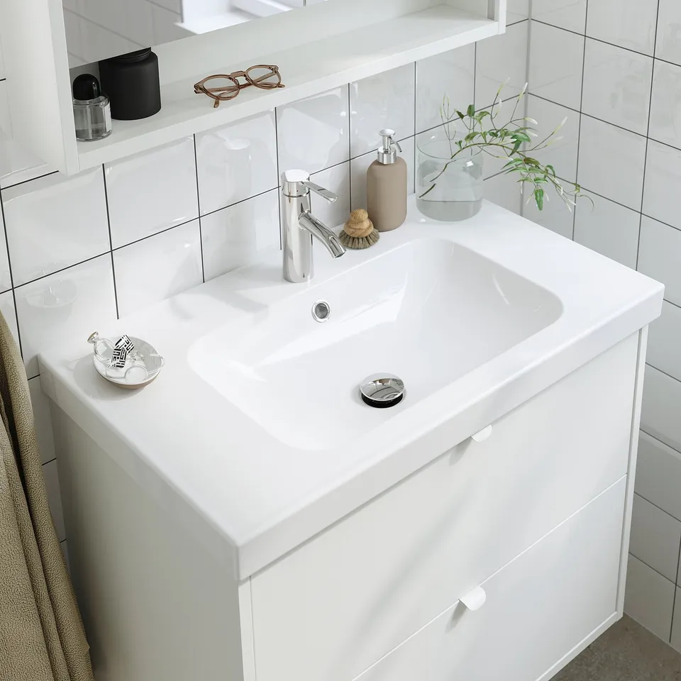 Modern bathroom sink with chrome tap, soap dispenser, plant, and toothbrush holder on a white counter.