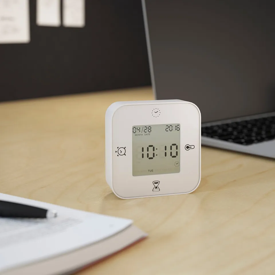 Digital clock at 10:10 on desk near laptop and papers.