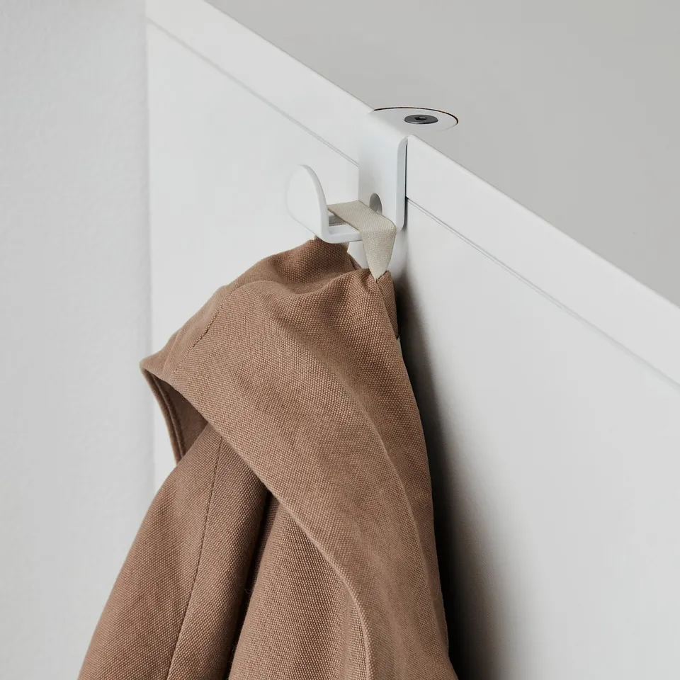 Brown coat hangs on white hook attached to a white cabinet fixed into a white ceiling.