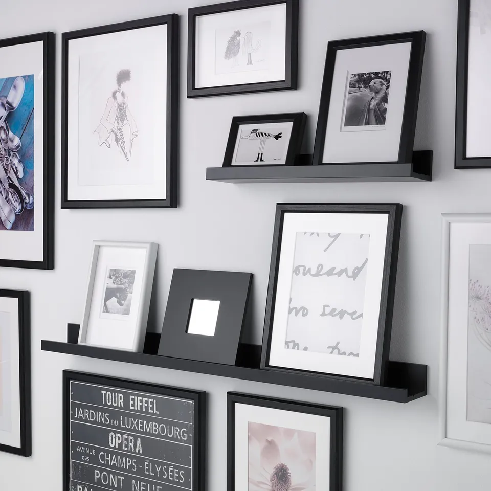 Wall covered with multiple framed pictures and two black picture ledges displaying photos and art.