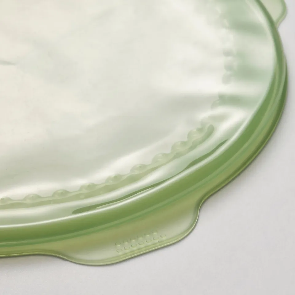 Green silicone rubber food cover, textured edge, transparent surface, soft to touch.