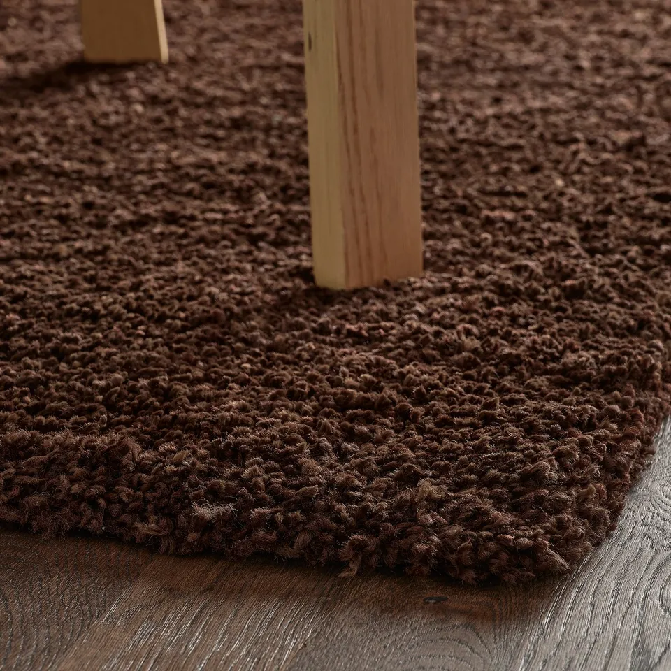 Shaggy brown rug on wooden floor. Soft, dampens sound, durable.