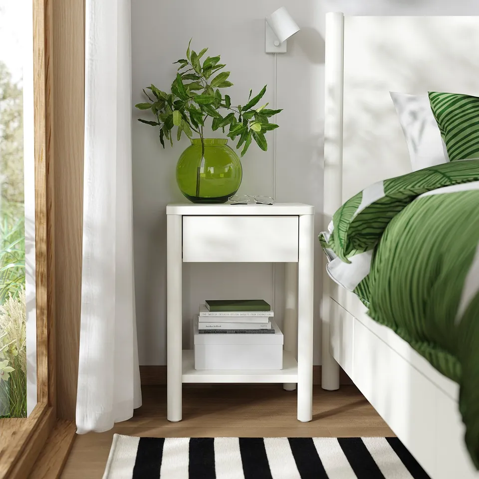 TONSTAD off-white bedside table with storage; fits neatly beside large bed, holds books & vase with green leaves.