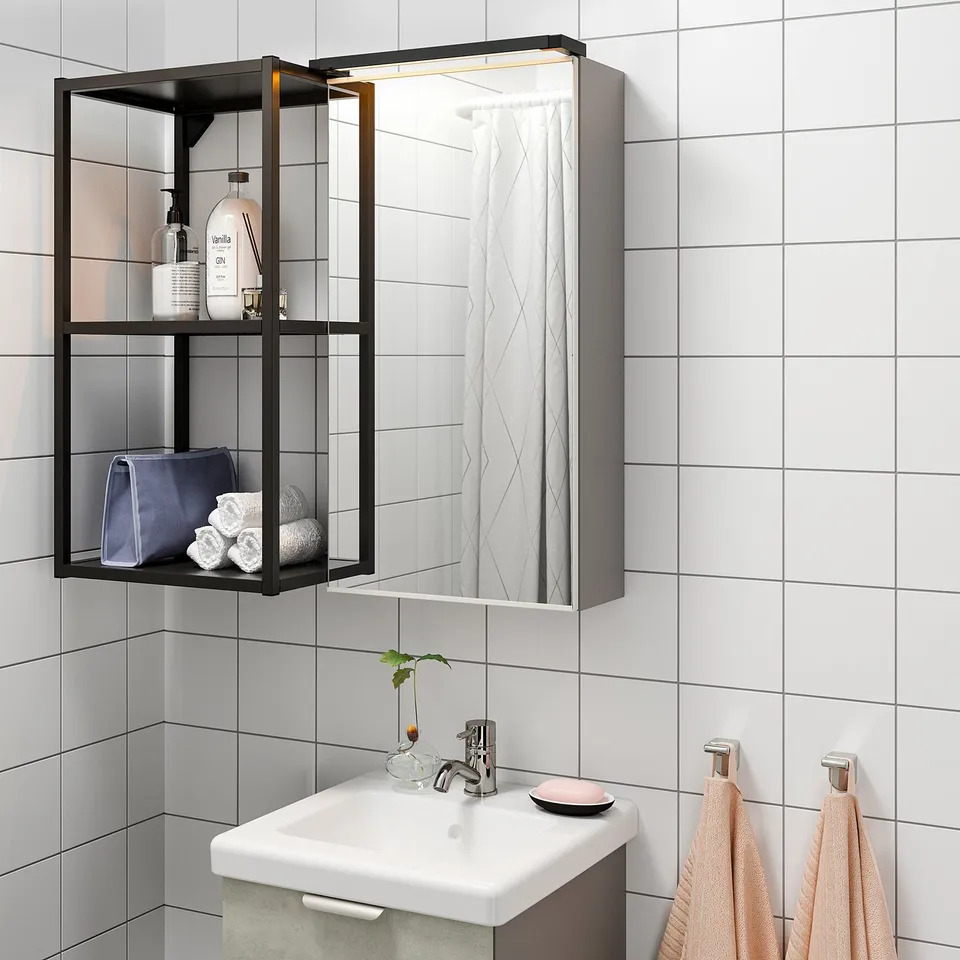 Modern bathroom with wall-mounted mirror cabinet featuring led lights, reflecting towels, bottles, and a sink.