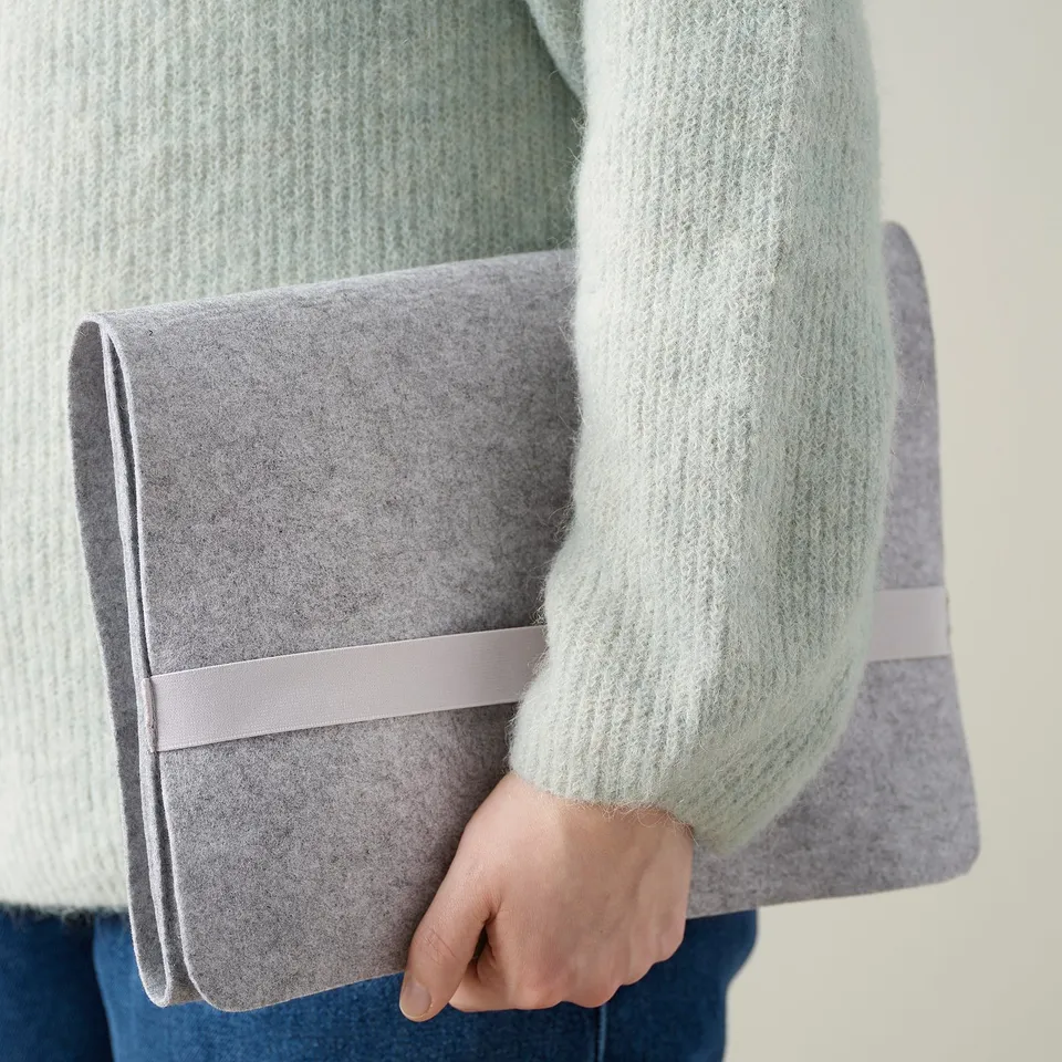Person holding grey felt clutch, wearing mint green sweater.
