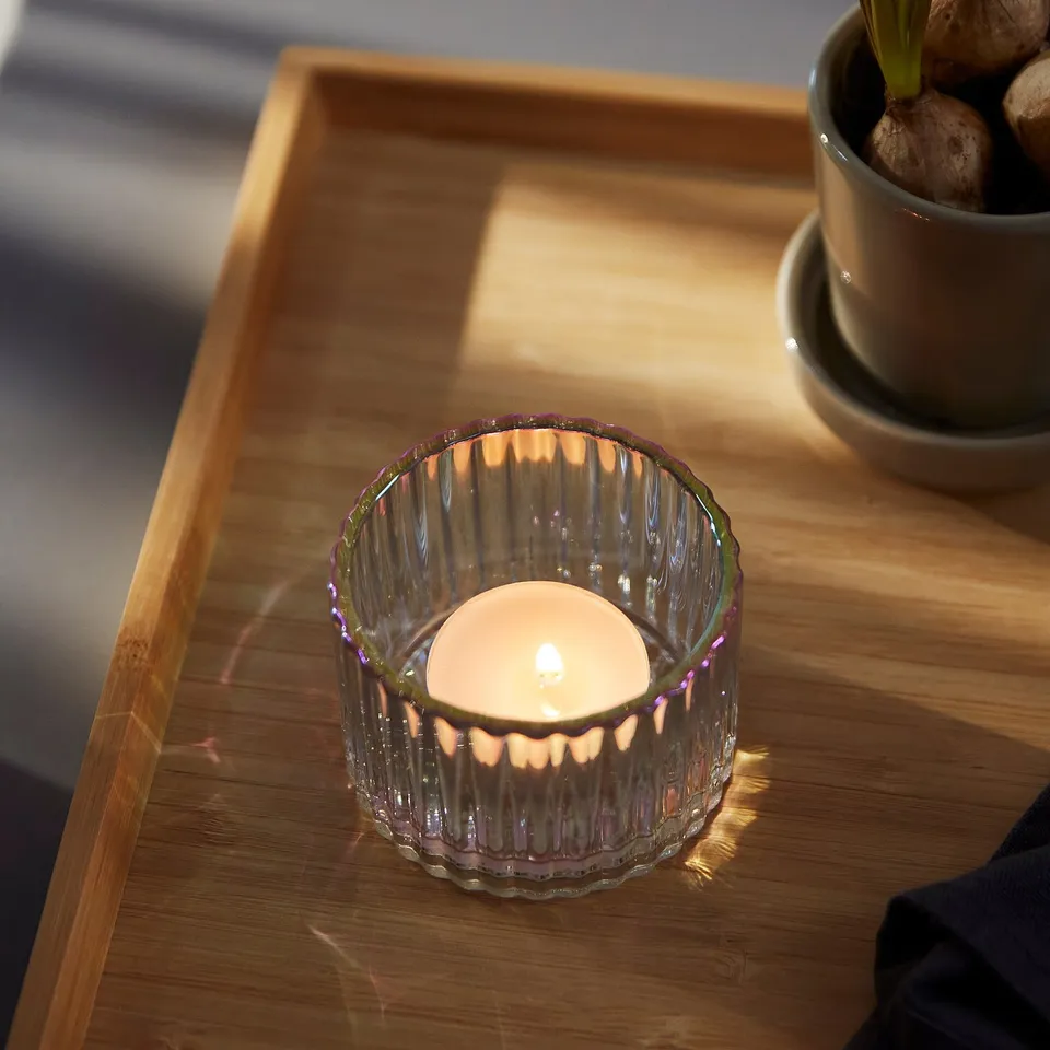 Mother-of-pearl glass candle holder with grooved pattern on wooden table, lit candle.