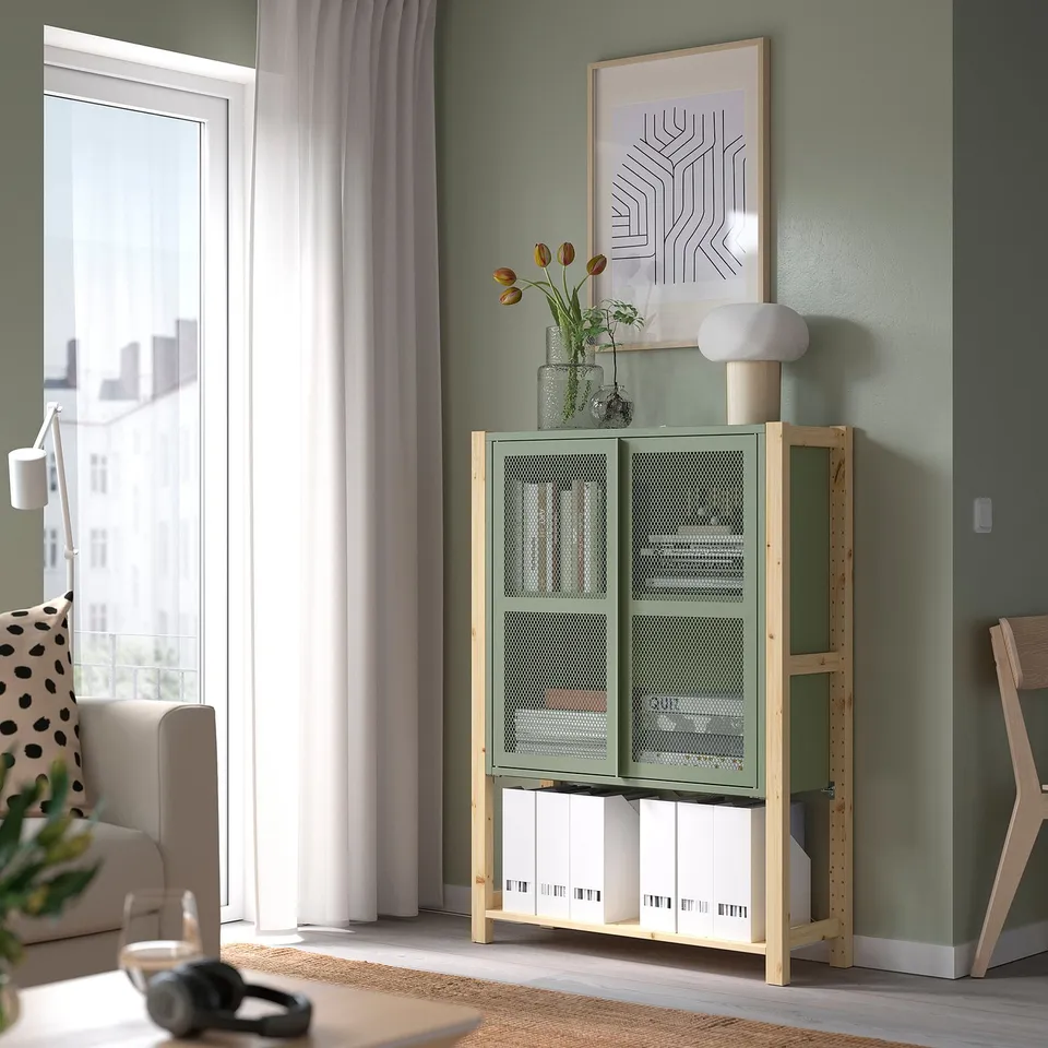 Green IVAR unit near window, holding boxes and vase with flowers.