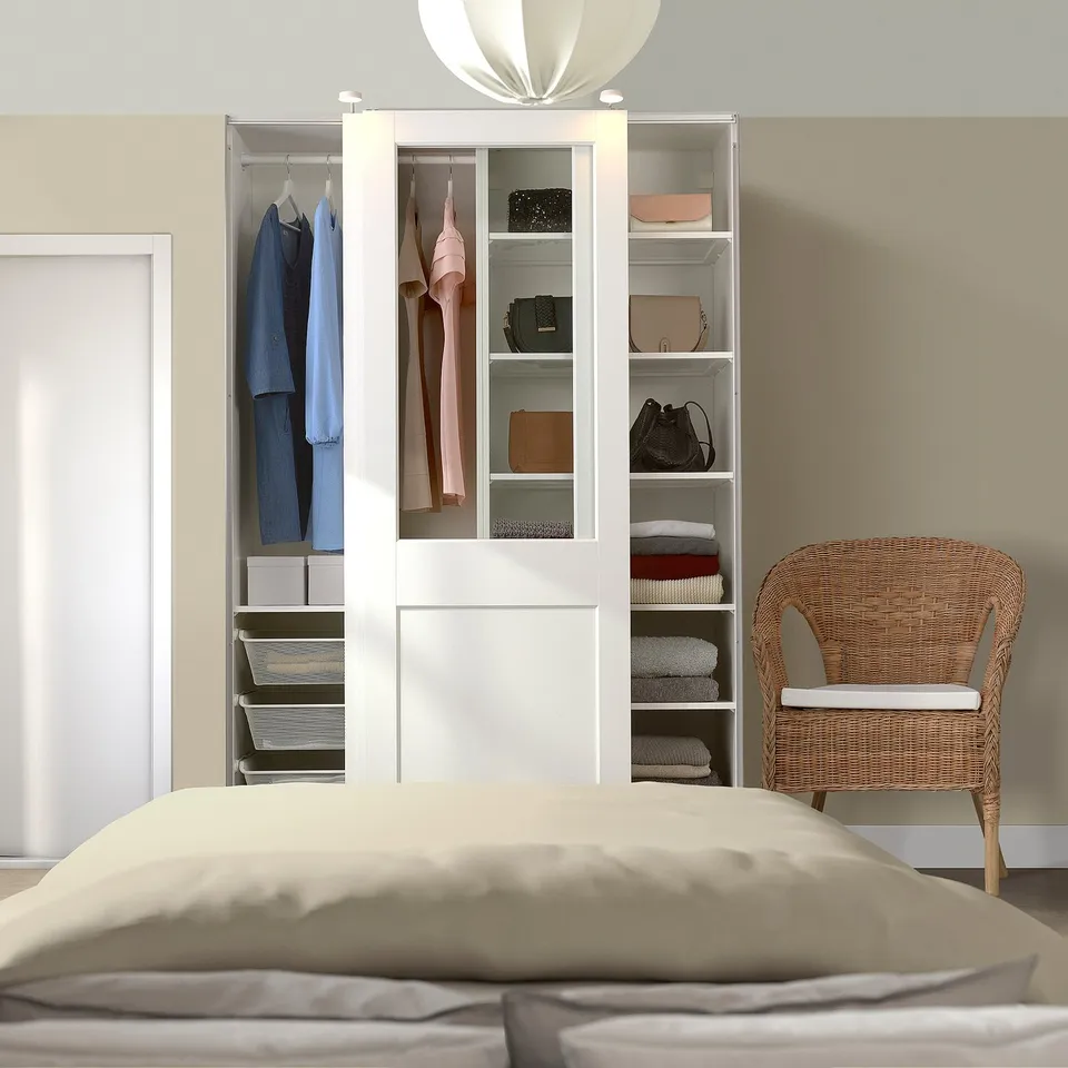 Modern bedroom with PAX wardrobe, clothes, and wicker chair.