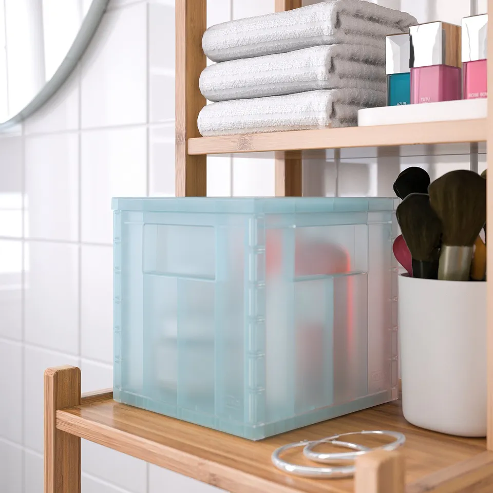 A bathroom shelf with a light blue storage box, towels, makeup, and brushes. The box keeps items organised and visible.