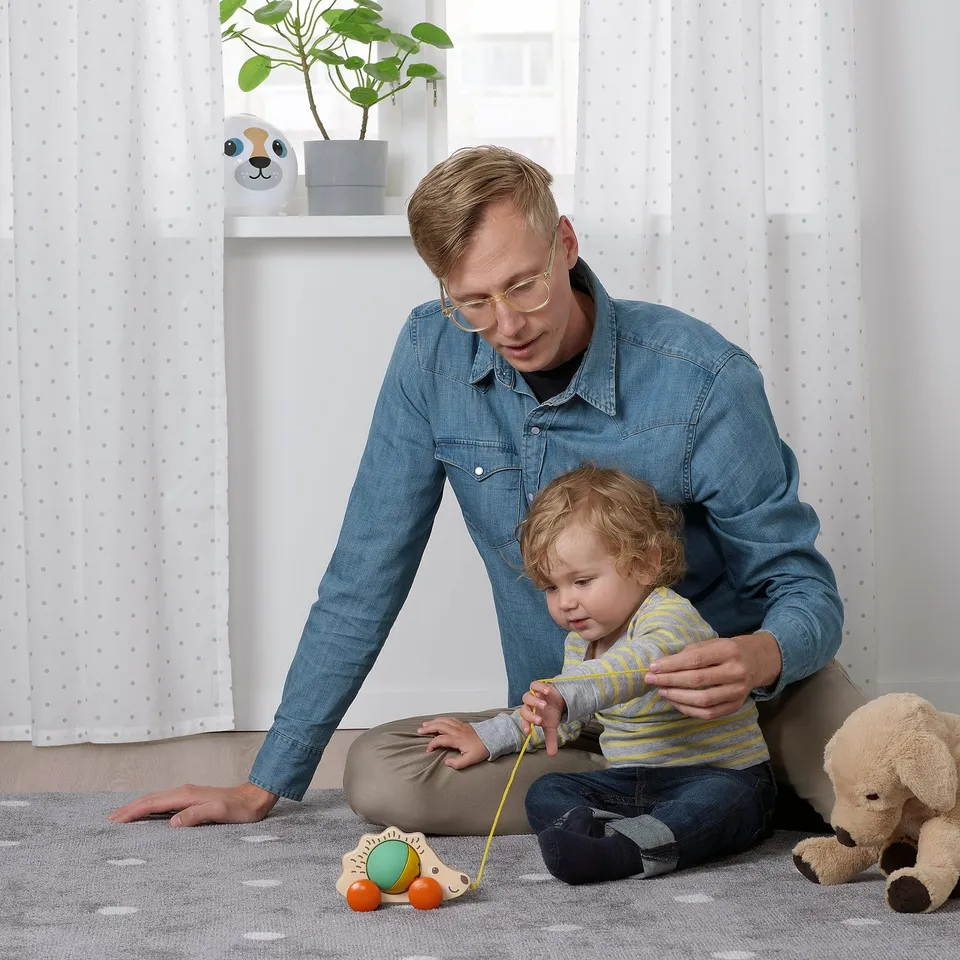Person plays with toddler and toy hedgehog. Teddy bear nearby.