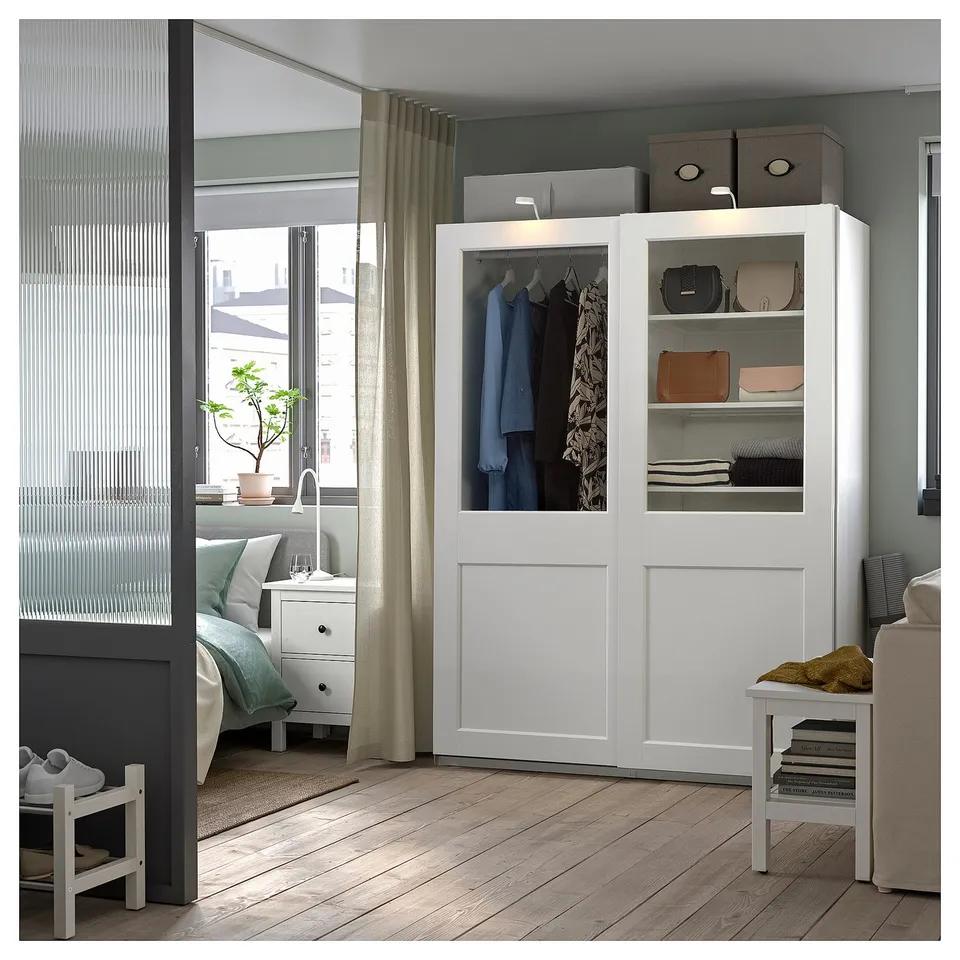 A modern, white PAX wardrobe with glass doors displays clothes and stores items neatly.