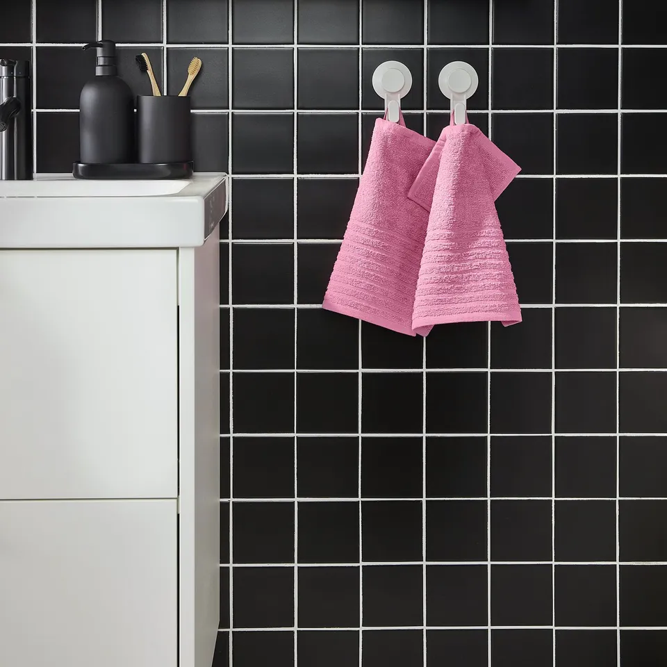 Modern bathroom with white sink, black-tiled wall, pink VÅGSJÖN towels, black soap dispenser.